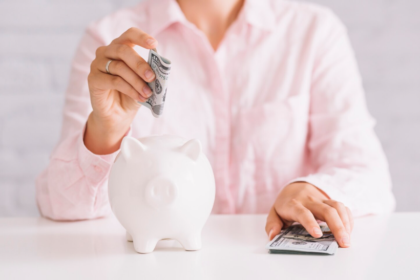 Person putting cash into a piggy bank as an example of easy ways to save money daily.