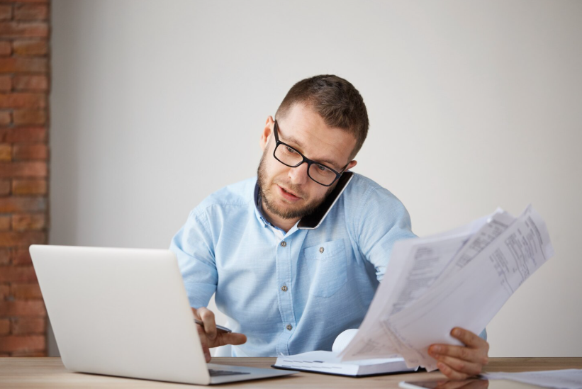 Man reviewing bills and negotiating monthly charges over the phone at his laptop.