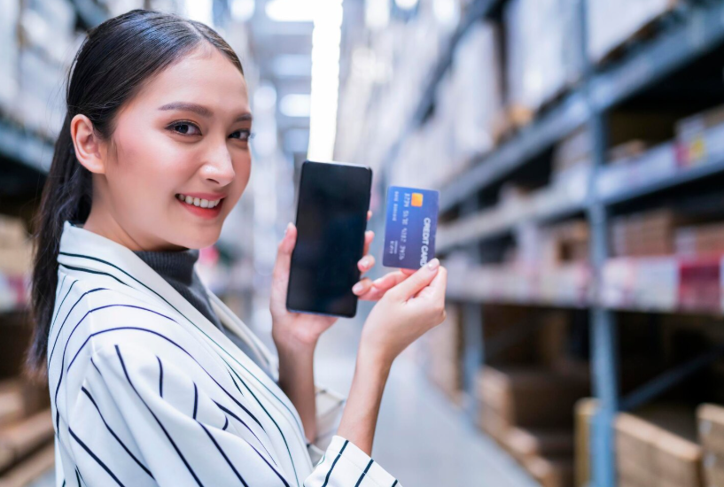 Woman using a phone and credit card while shopping in a warehouse club without a membership.